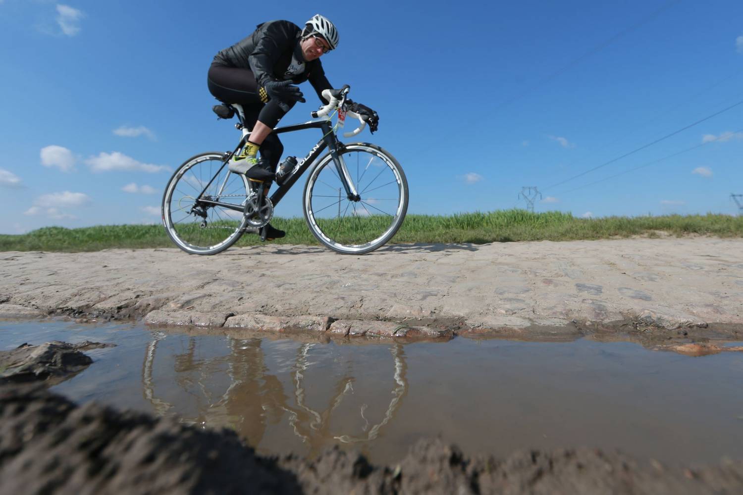 A rider is reflected by puddles on the Grand Depart 2025